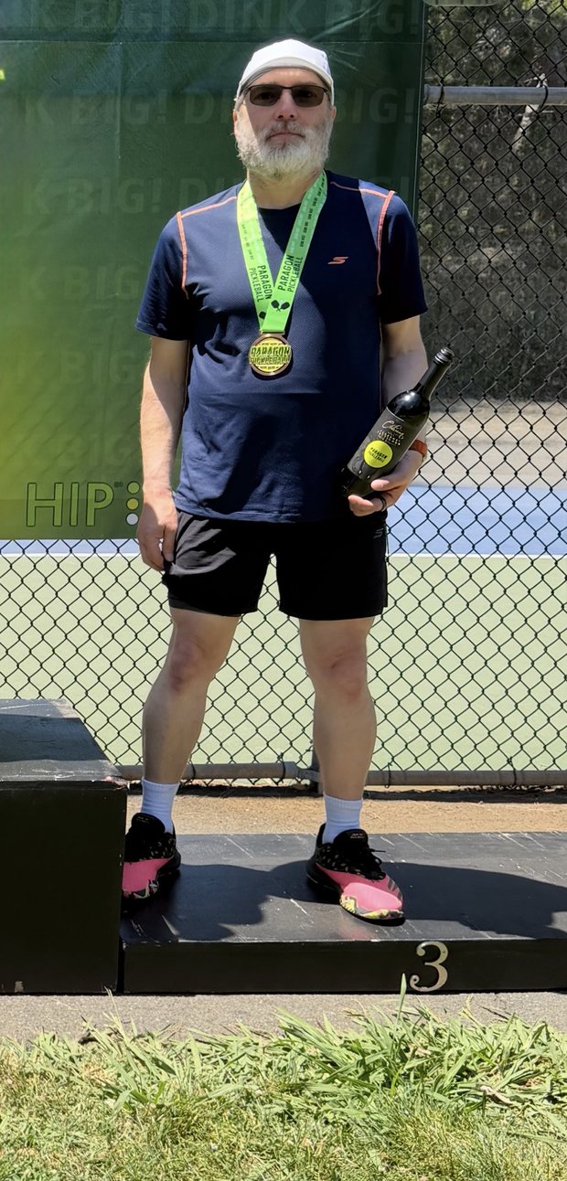 The scout on the third-place step of a podium, wearing a medal and holding a bottle of wine